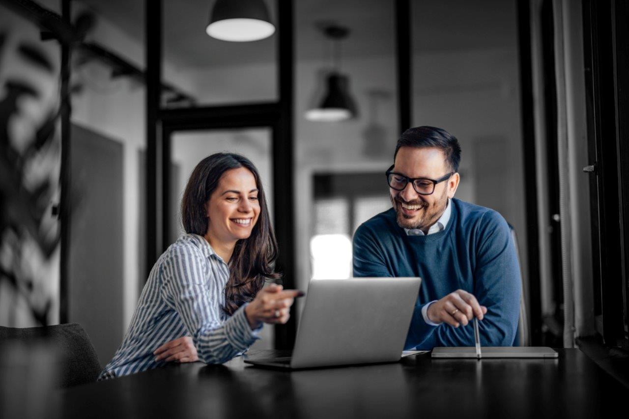 Two young business people looking at laptop and smiling.
